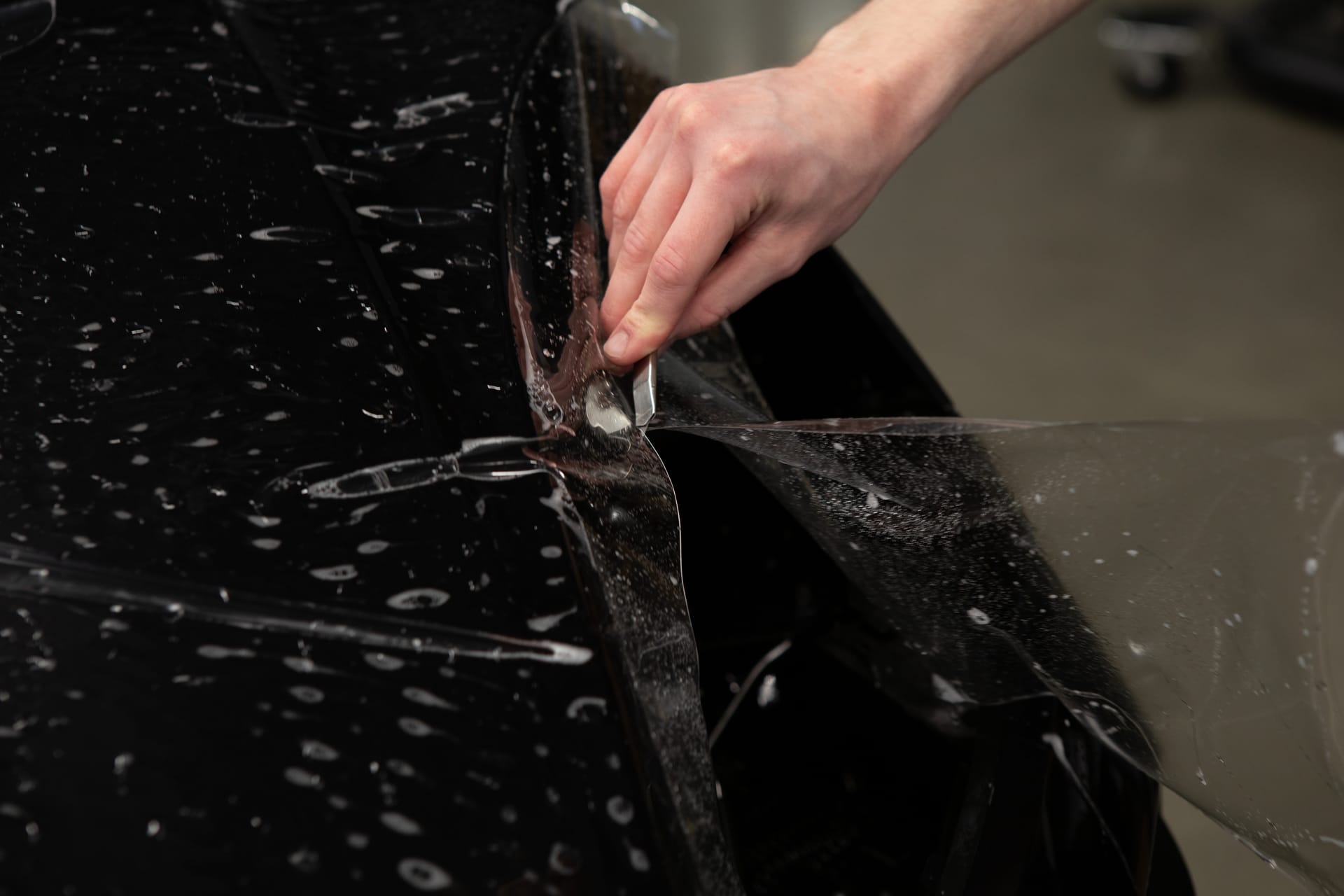 Macro detail of STEK paint protection film lifting off a dark panel.