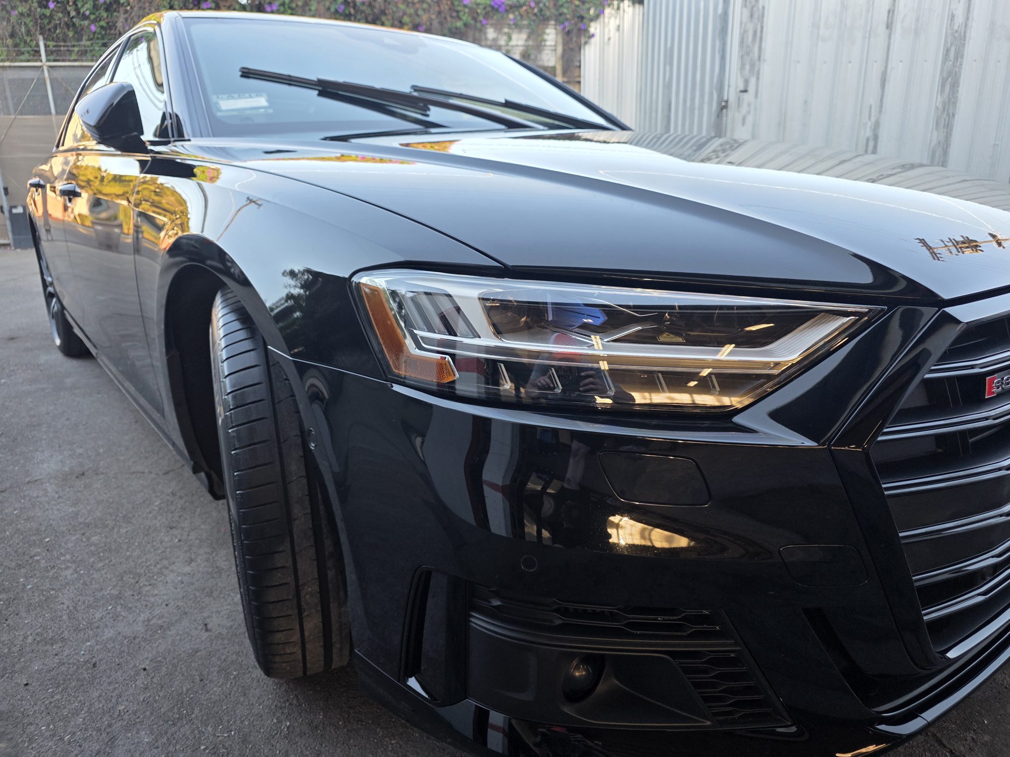 Headlight and fender detail on a black Audi S8 after ceramic coating, the paint reading as a clean mirror of the sky.