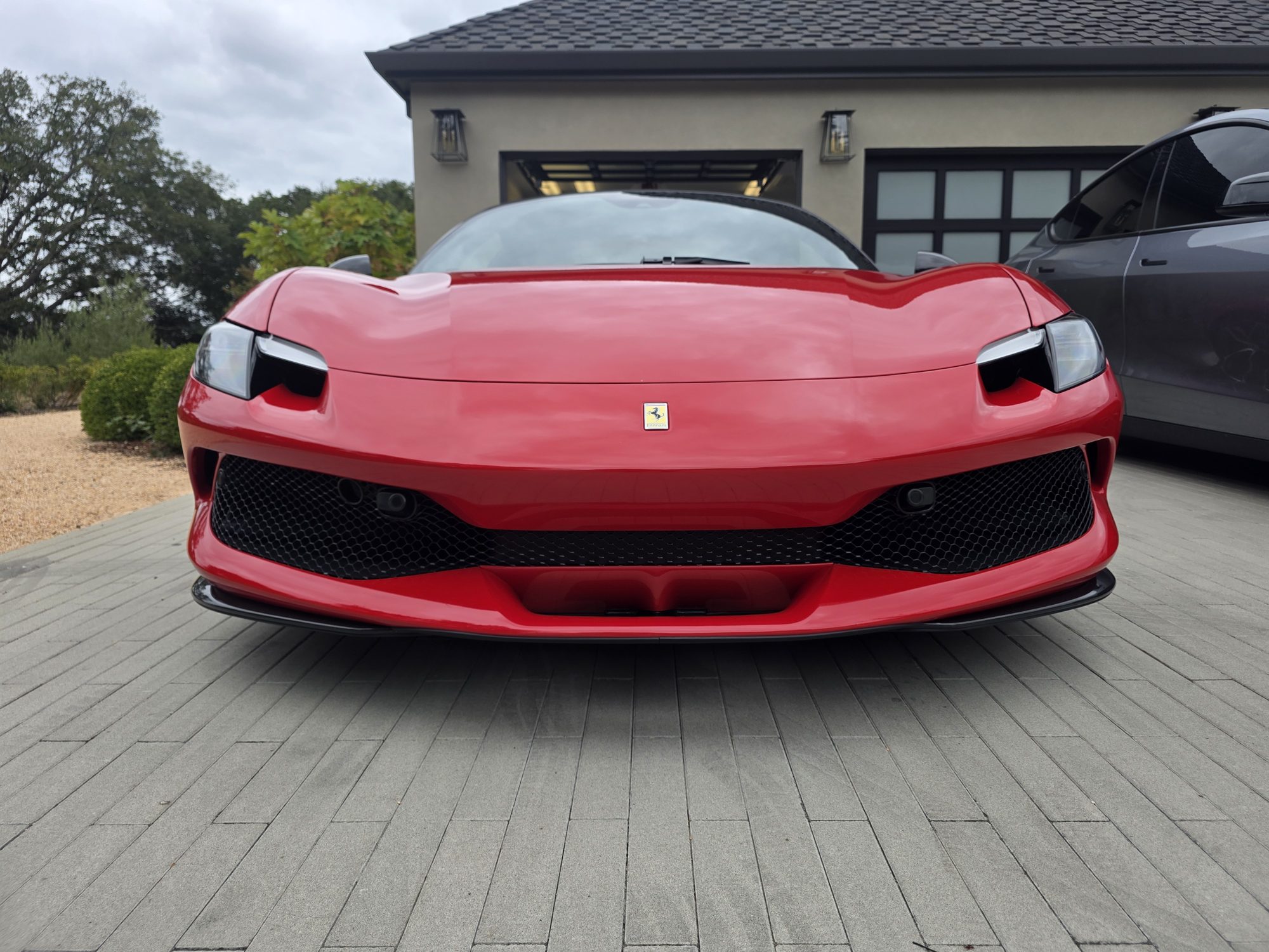 Straight-on front view of a ceramic-coated red Ferrari 296 GTS in front of the owner's garage.