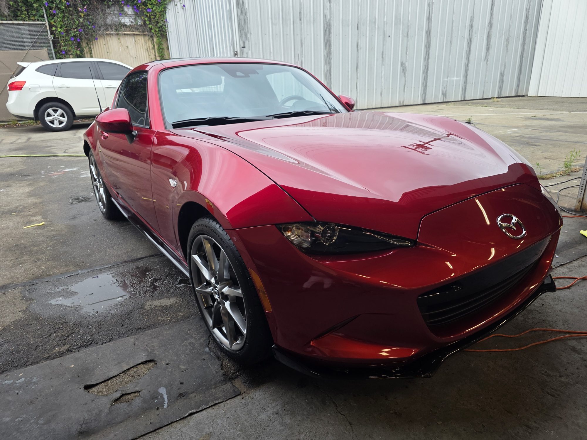 Front three-quarter view of a ceramic-coated red Mazda MX-5 RF, the hood curves reflecting the shop wall.