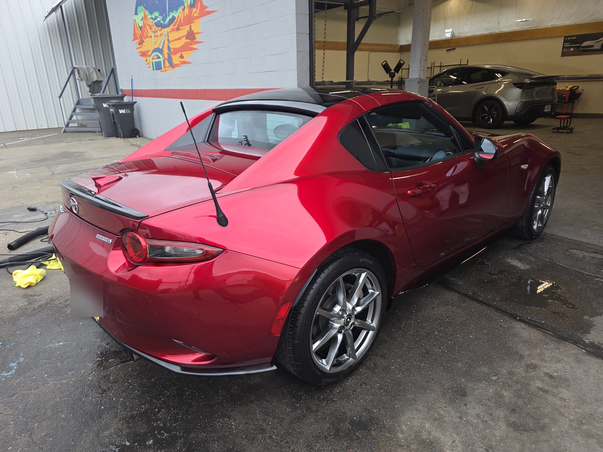 Rear three-quarter view of a red Mazda MX-5 RF after ceramic coating, the fastback roof and rear quarter in the shop doorway.