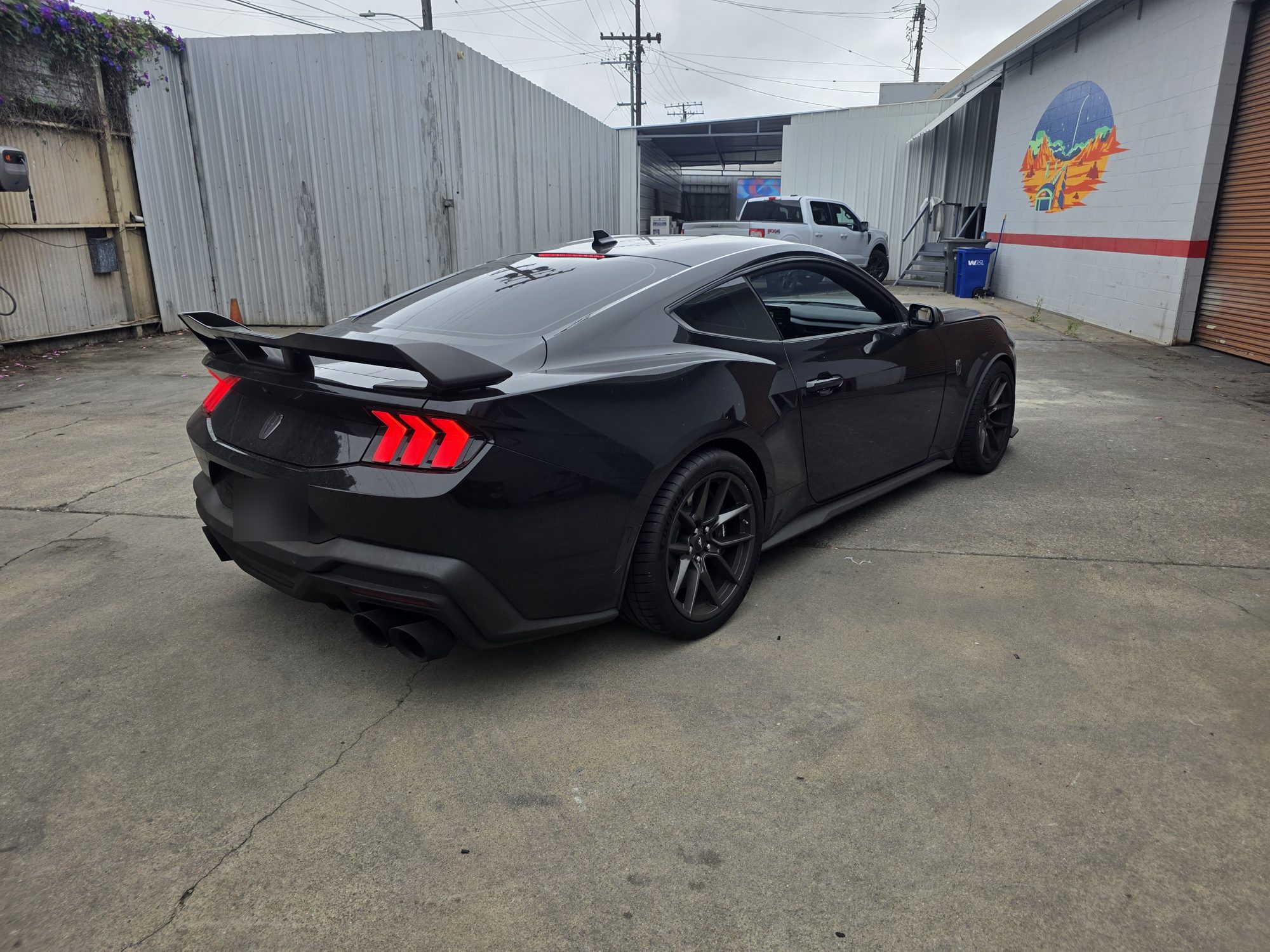 Rear three-quarter view of a ceramic-coated black Mustang Dark Horse with the rear wing, tail lights lit.