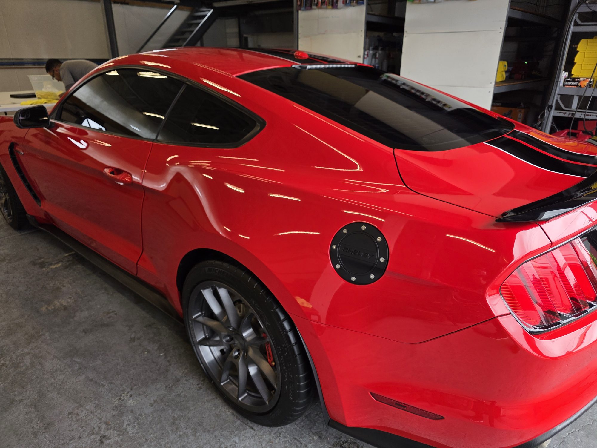 Rear three-quarter view of a red Shelby GT350 after ceramic coating, the door and quarter panel reflecting the shop ceiling lights.