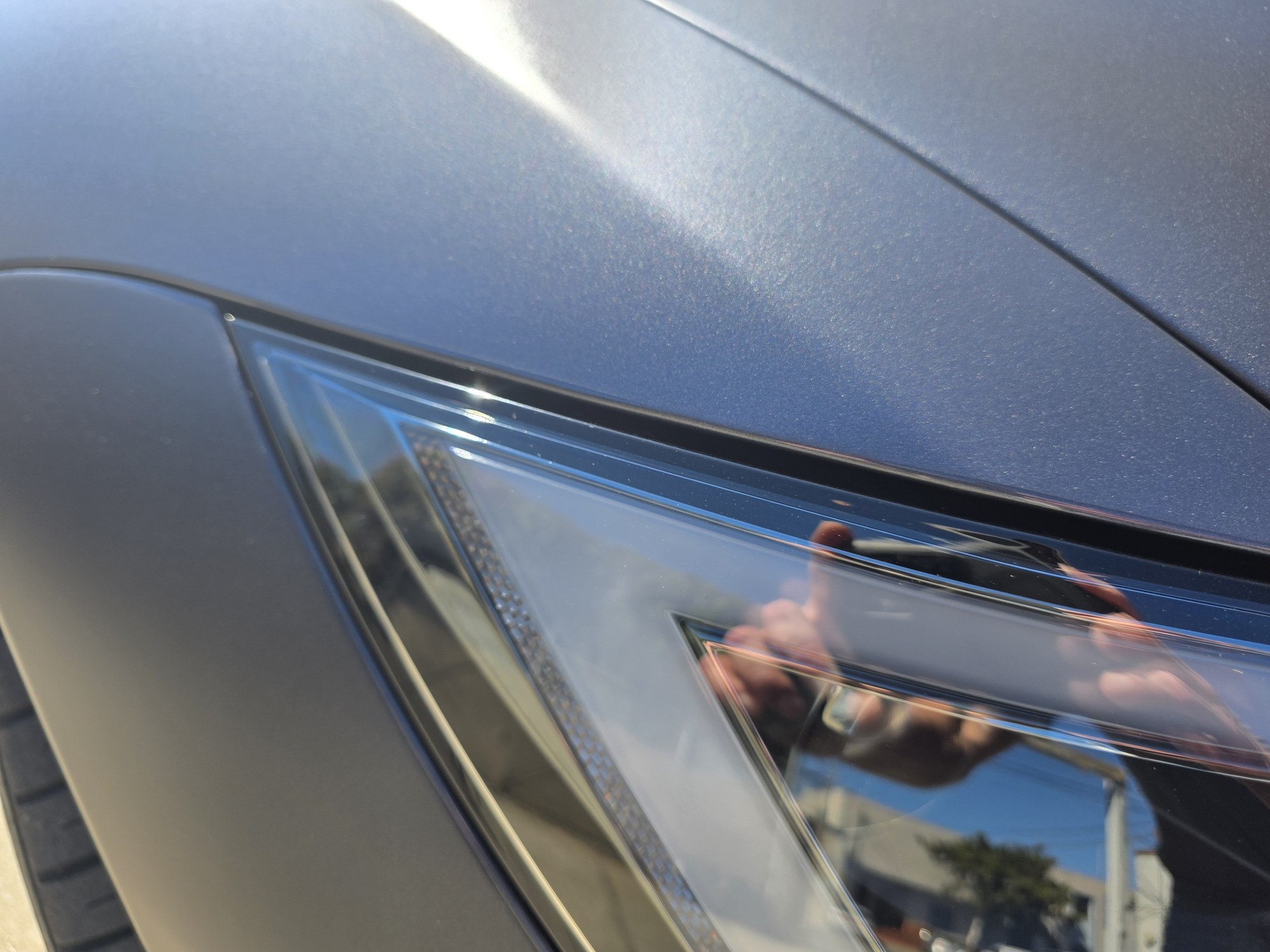 Close-up of the headlight seam on a satin grey Tesla Model S after a full-body STEK DYNOmatte paint protection film install: the film edge is tucked along the lens with no visible line.