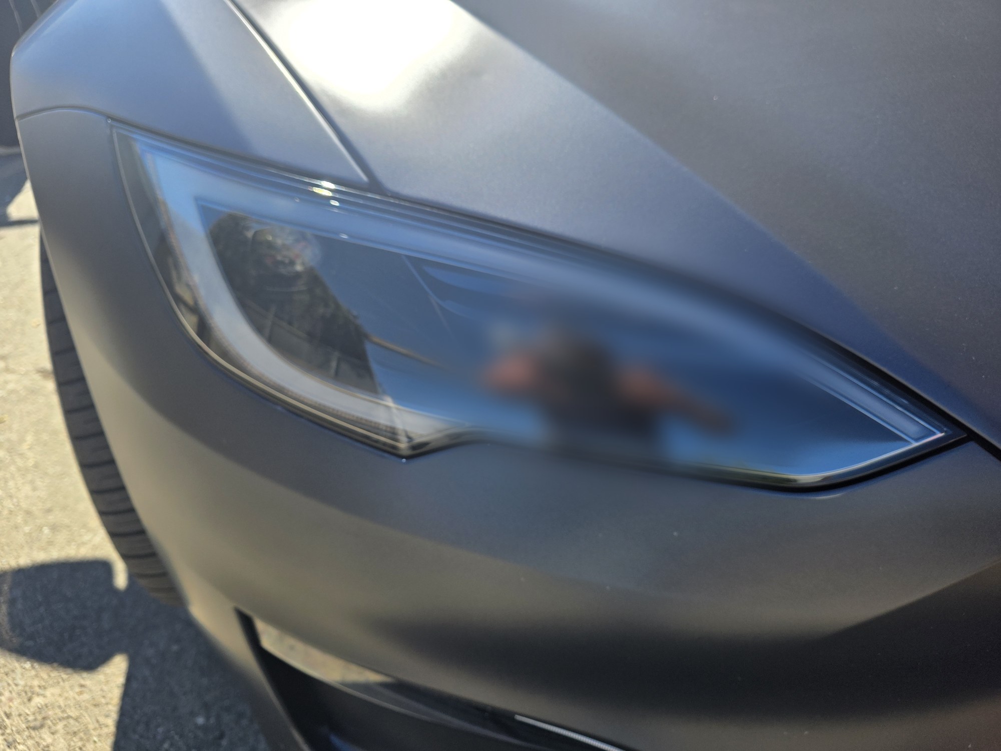 Headlight and fender of a Tesla Model S in matte paint protection film, the satin surface meeting the clear lens cleanly, photographed in direct sun outside the Innovo shop in Oakland.