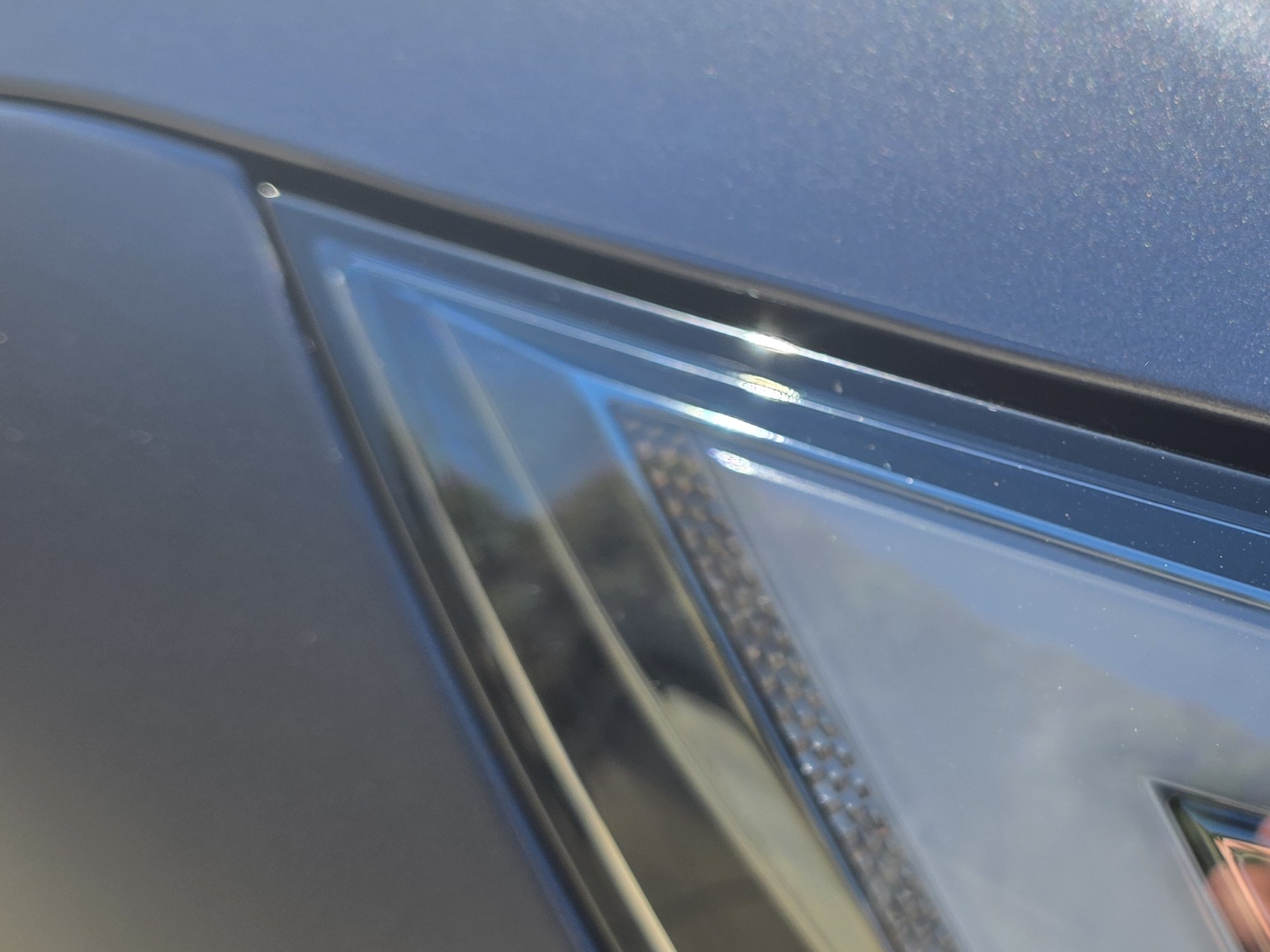 Detail of the hood-to-headlight gap on a Tesla Model S in STEK DYNOmatte film, the film trimmed to the panel gap and tucked, the satin texture visible in direct sun.