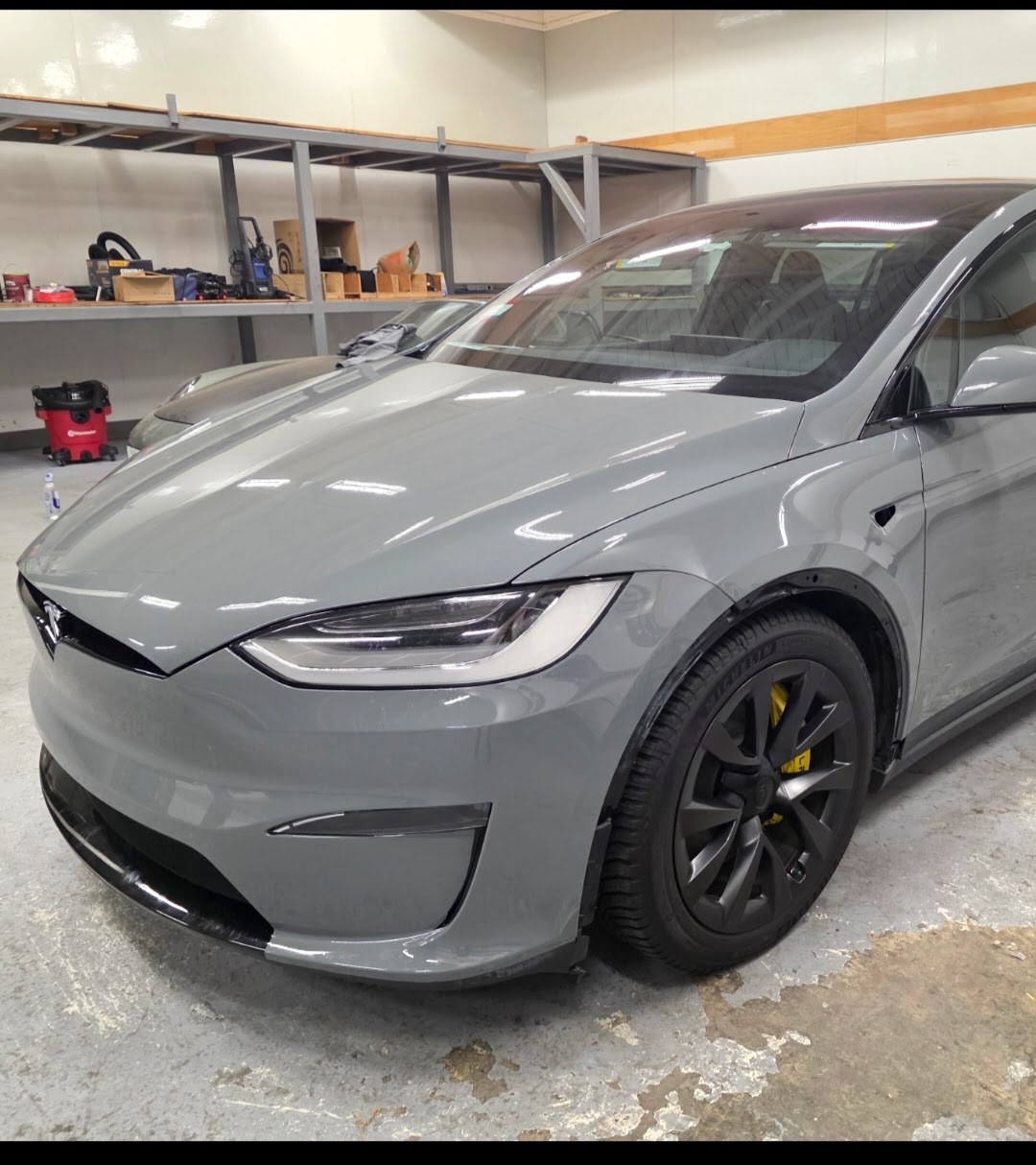 Tesla Model X in satin grey STEK DYNOgrey colour-change paint protection film after the install, front three-quarter view in the Innovo shop in Oakland, yellow-wrapped brake caliper visible behind the wheel.