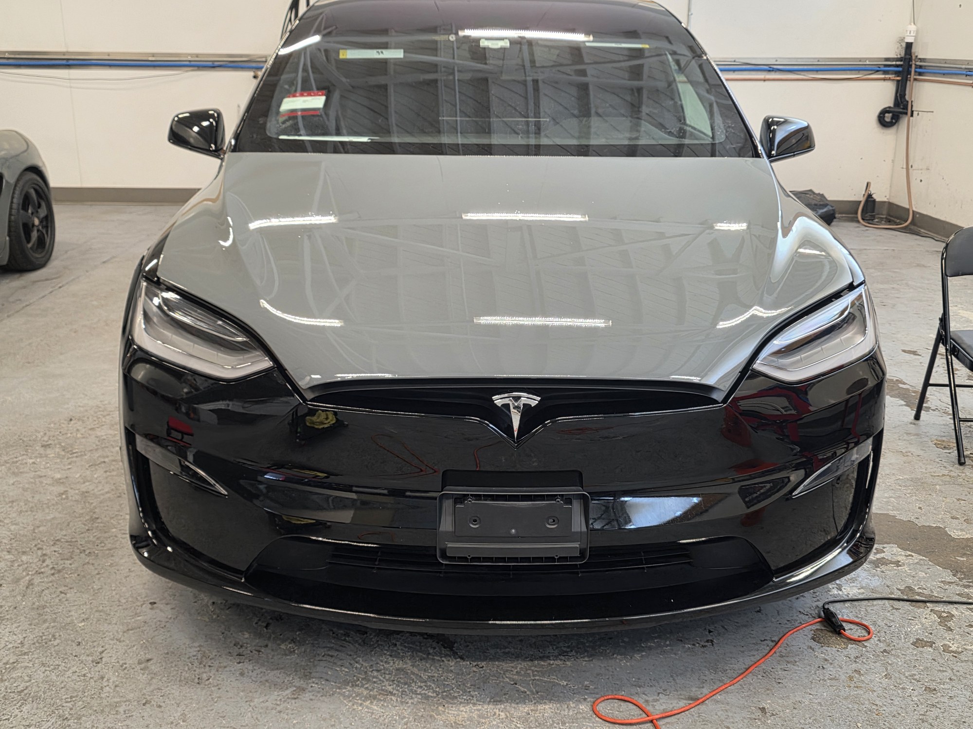 Tesla Model X halfway through a colour-change film install: the hood already in grey STEK DYNOgrey film, the fenders and bumper still factory black.