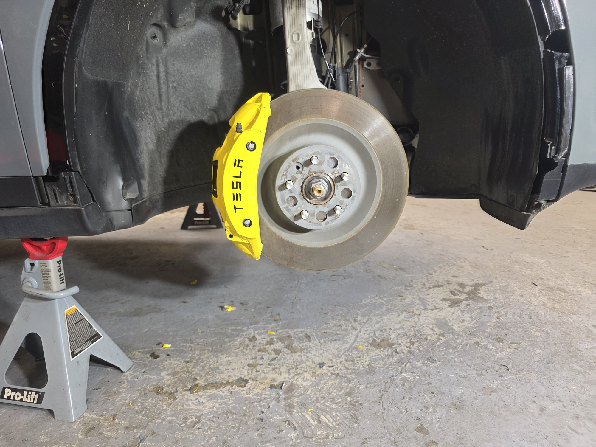 Tesla Model X brake caliper wrapped in yellow, wheel off, on a jack stand in the Innovo shop.
