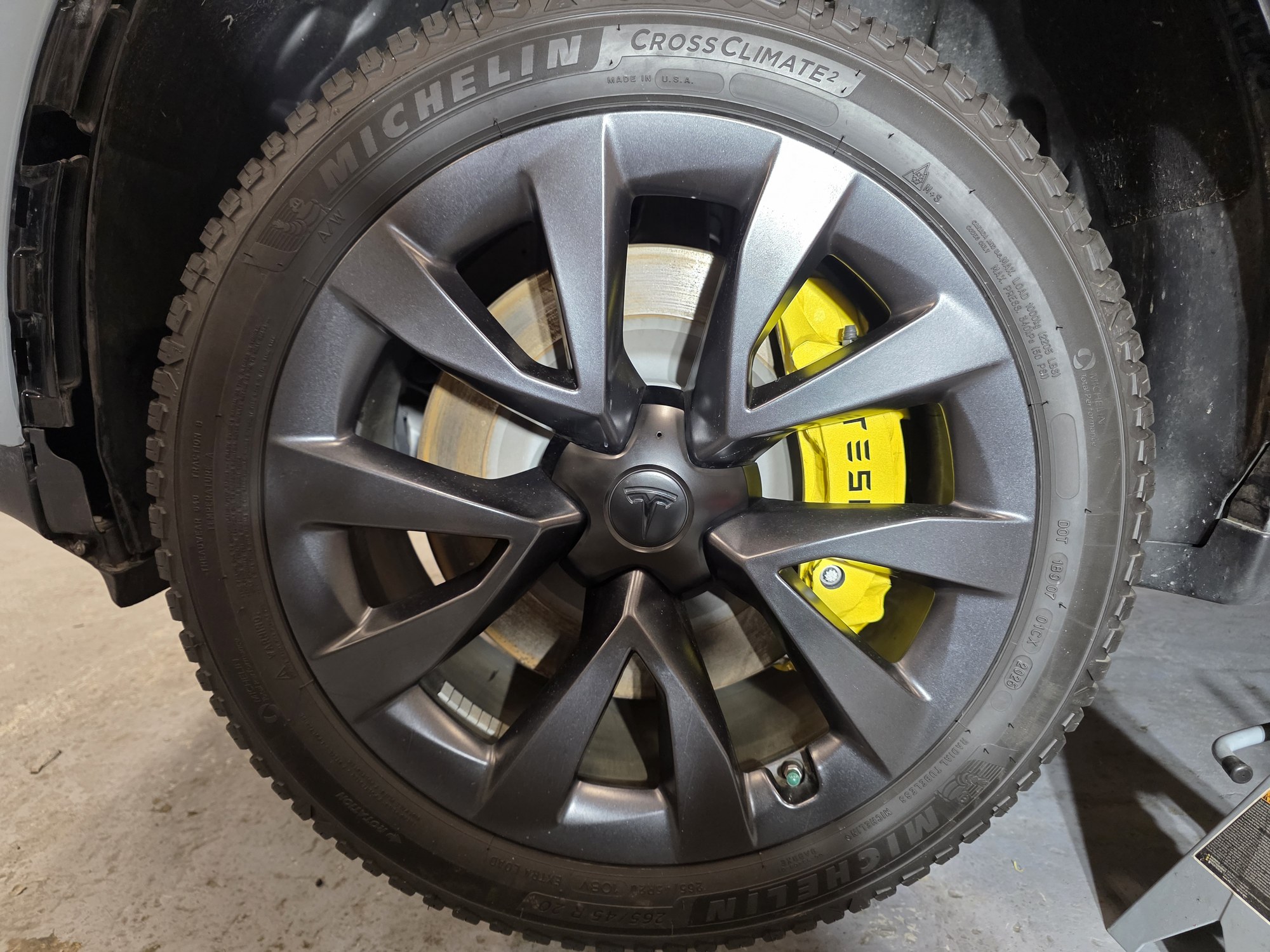Tesla Model X wheel back on, the yellow-wrapped caliper showing through the spokes.