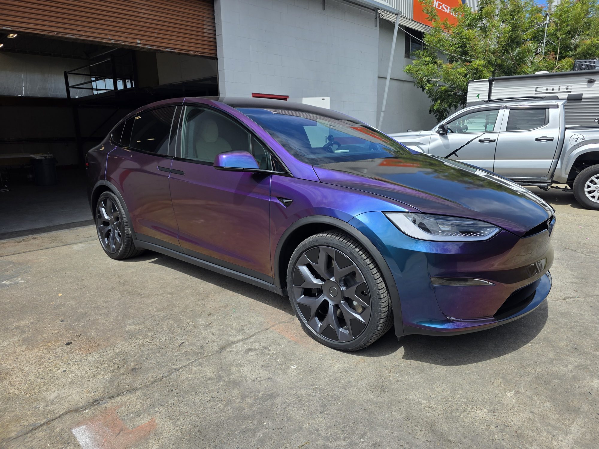 Driver-side front three-quarter view of a Tesla Model X, purple and blue colour-flip wrap under full-body clear paint protection film.