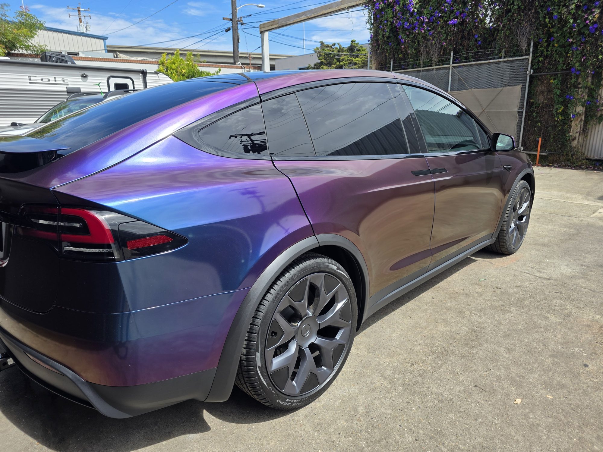 Rear three-quarter view of a wrapped Tesla Model X with clear PPF over the vinyl, the colour shifting from purple to blue across the quarter panel.